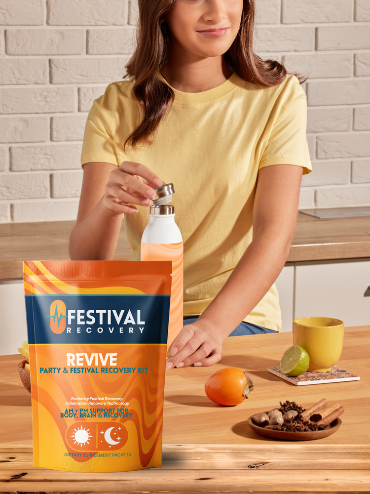 Woman at a kitchen counter holding a water bottle next to an orange Festival Recovery REVIVE kit pouch