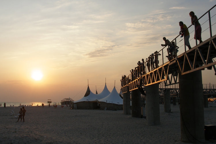 Festival goers on a pier above the beach as the sun sits low over the sea
